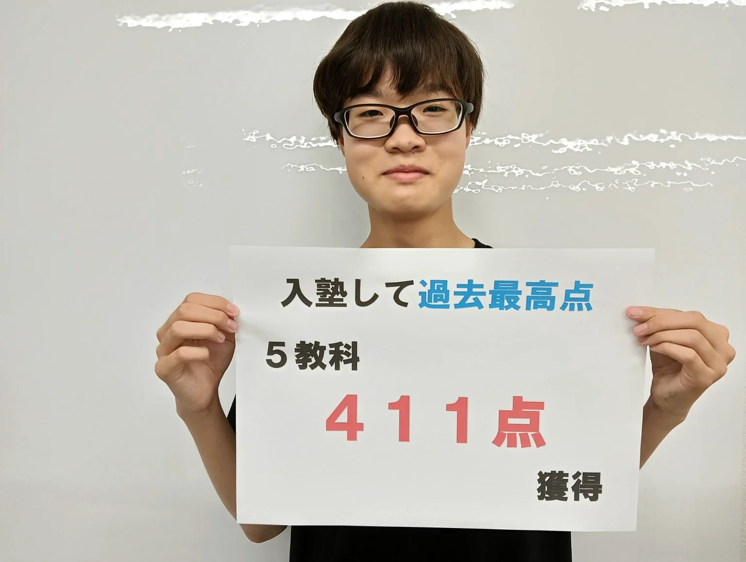 入塾後、過去最高点、5教科411点獲得と書かれたボードを持つ生徒