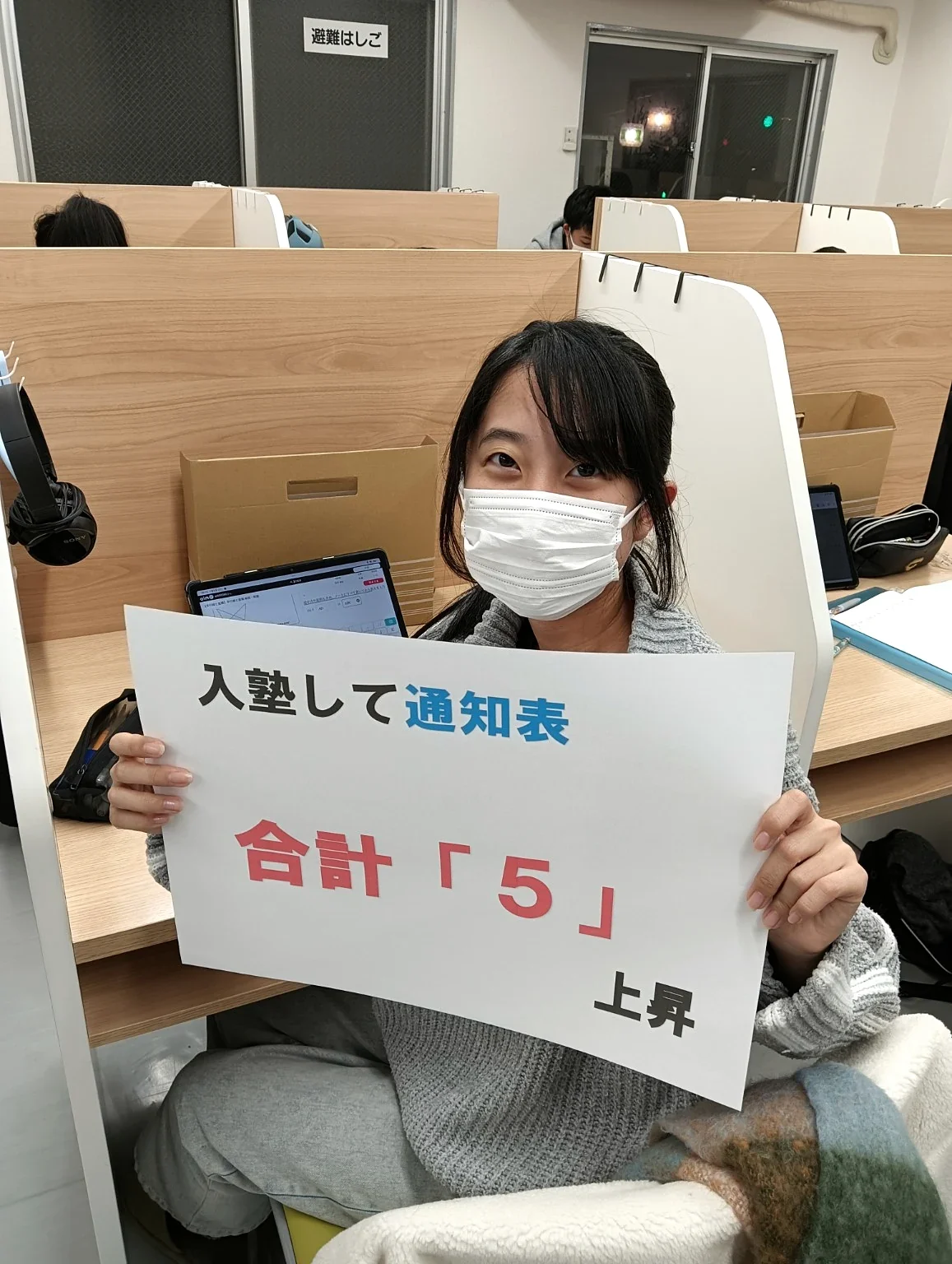 入塾後、通知表合計「5」上昇と書かれた実績ボードを持つ生徒