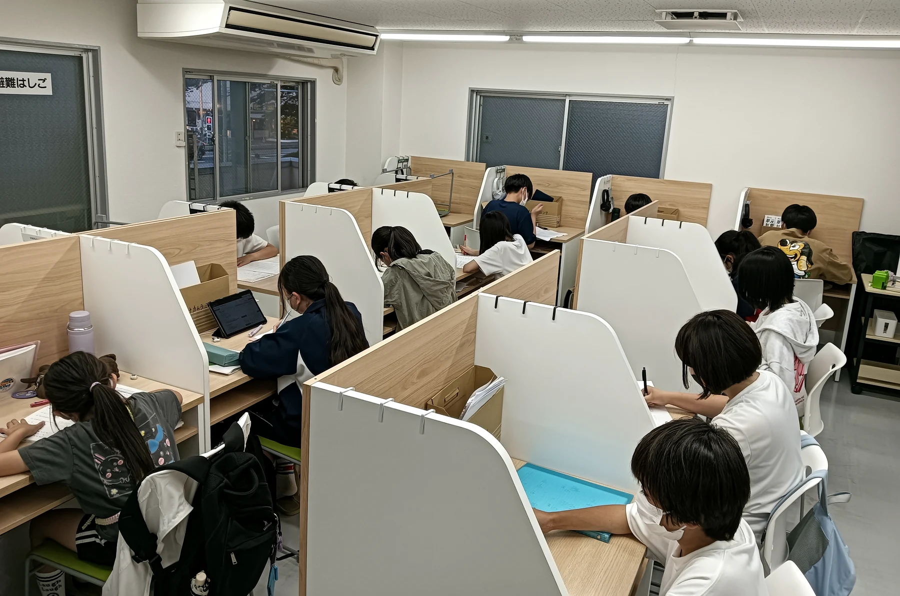 個別ブースでタブレットとノートを使って学ぶ生徒たち